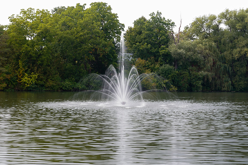 Floating fountain spraying in a park pond surrounded by trees