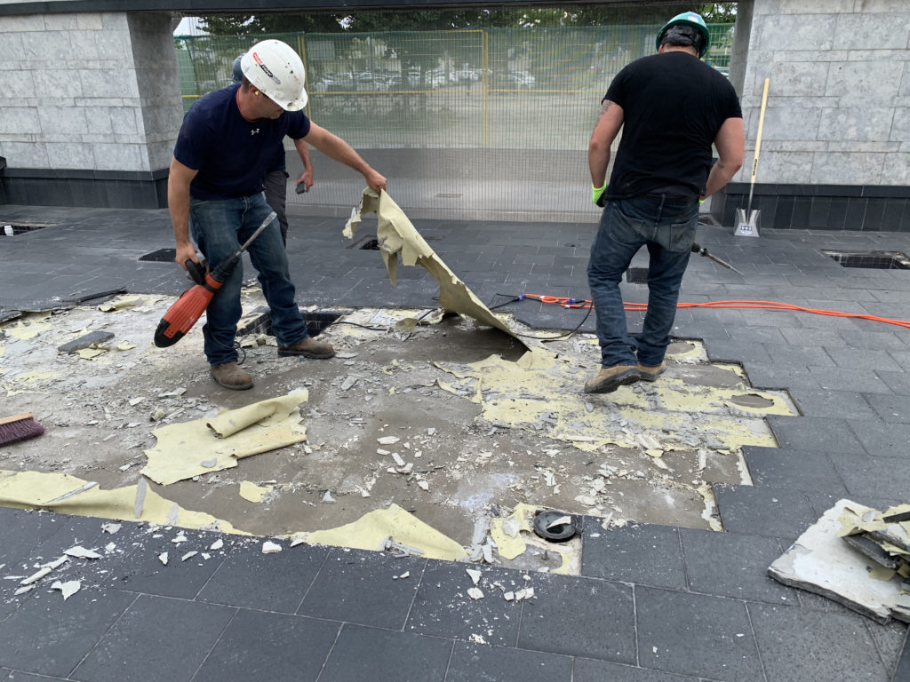 Worker pulling off failed waterproofing that should have been bonded to the concrete, likely installed on uncured concrete